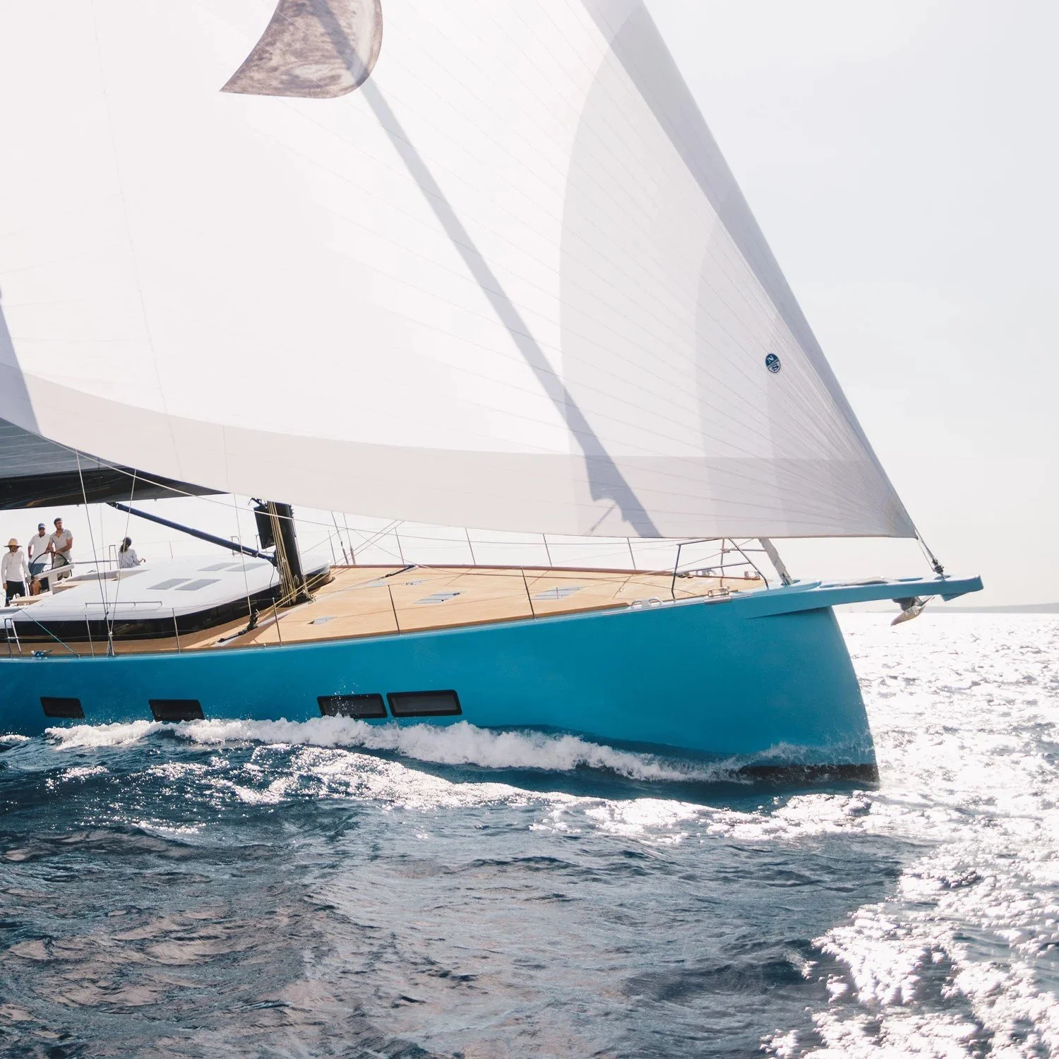 A blue sailboat with white sails on the water with a sunlight reflection on the surface.